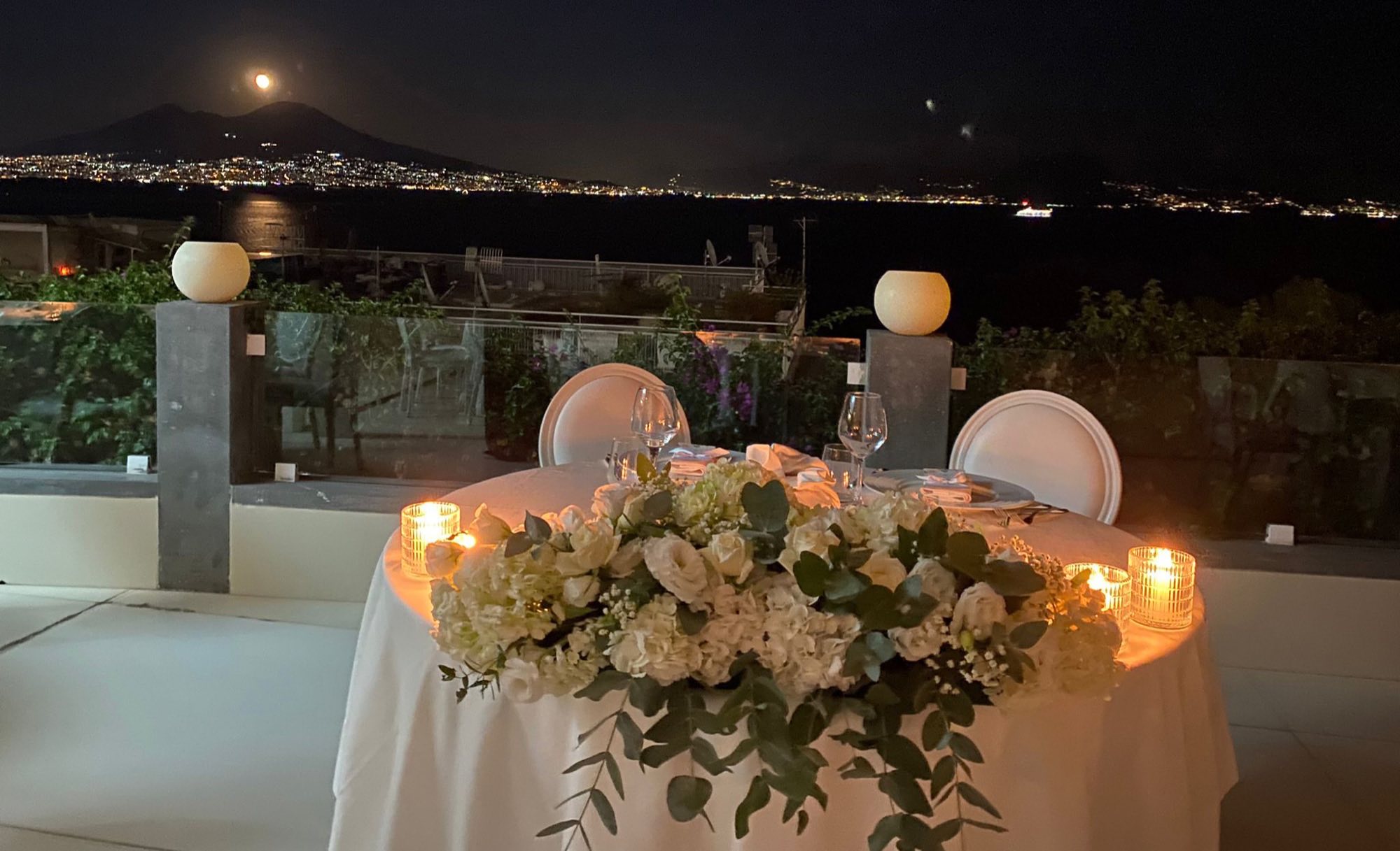 Tavolo degli sposi a lume di candela con il golfo illuminato di notte